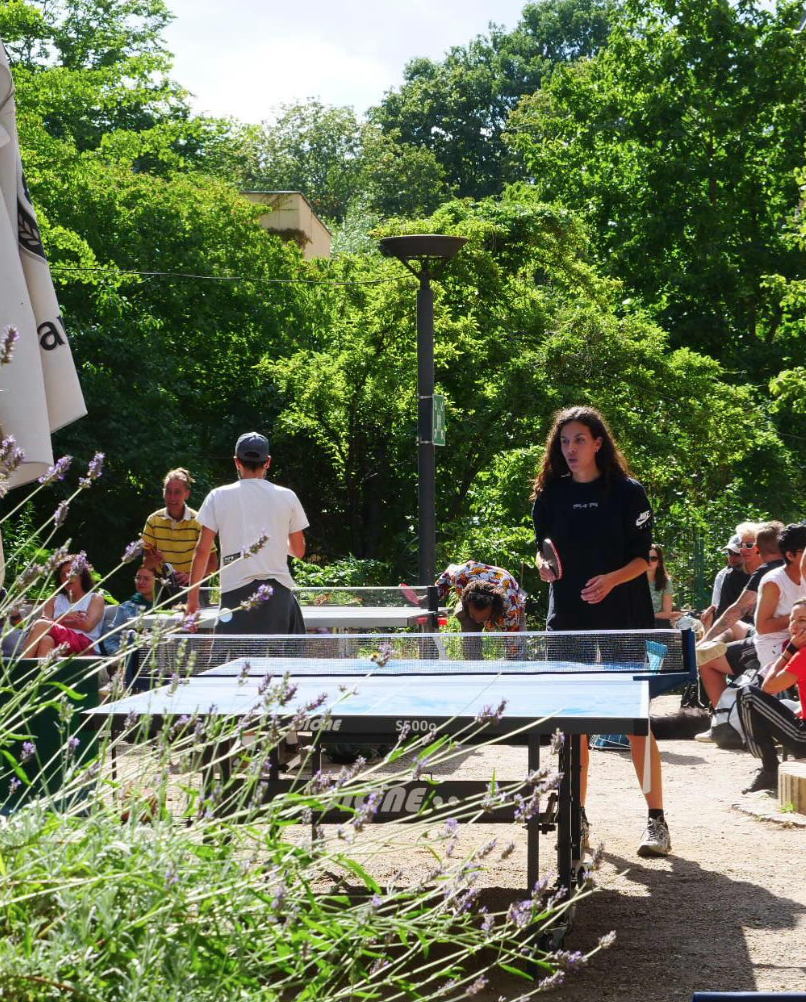 Here we see people playing ping pong outside on a sunny day.