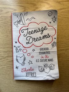 A photo of the cover of teenage dreams, which has stylized doodles on it and a lined paper background, evoking teen doodles in a notebook.